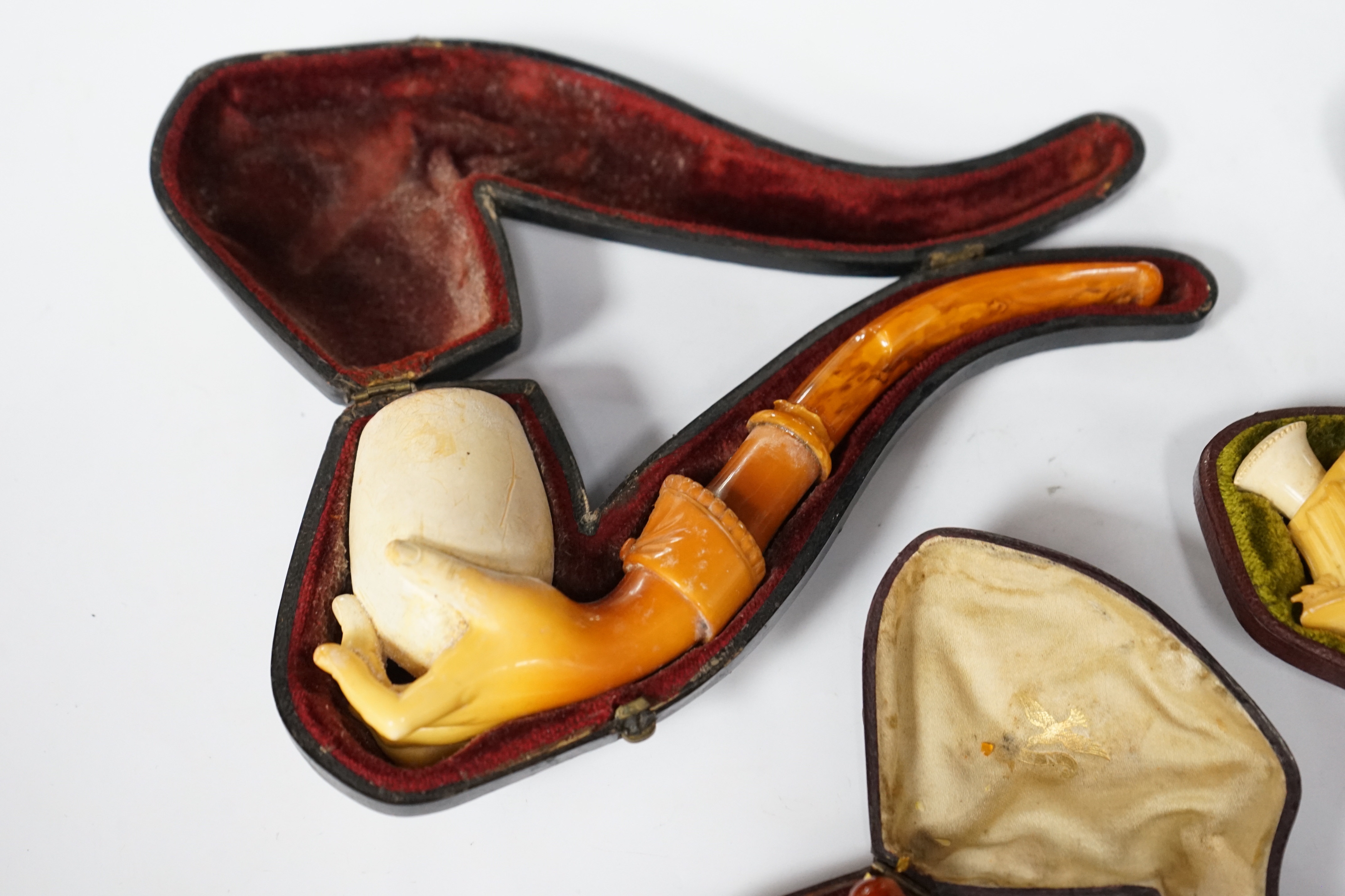 Three cased novelty Meerschaum pipes and pipe bowls, all with amber mouth pieces, one of a horses and cowboy, another a model of a hand and the other of a scantily clad lady wearing a riding cap, largest 17 cm long